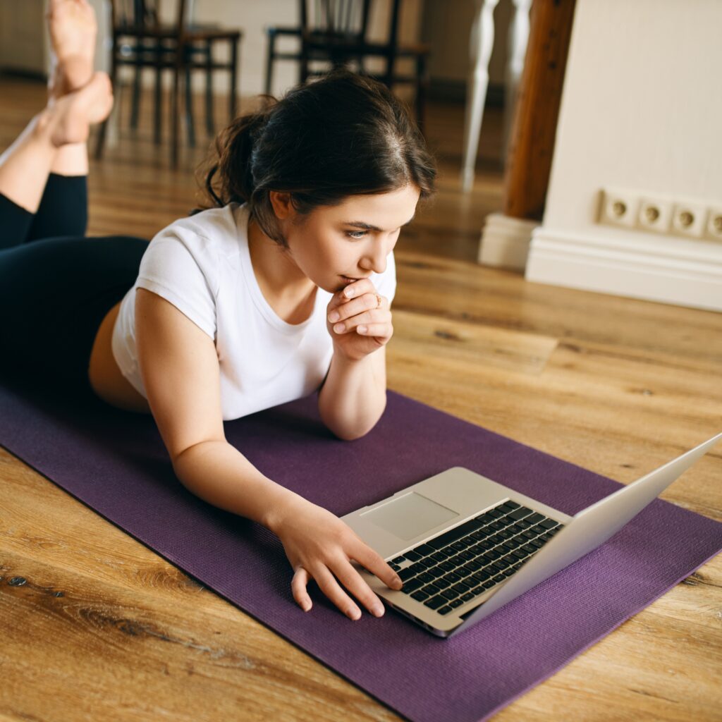 indoor image beautiful young woman with fit muscular body lying her stomach yoga mat surfing internet via laptop after home training
