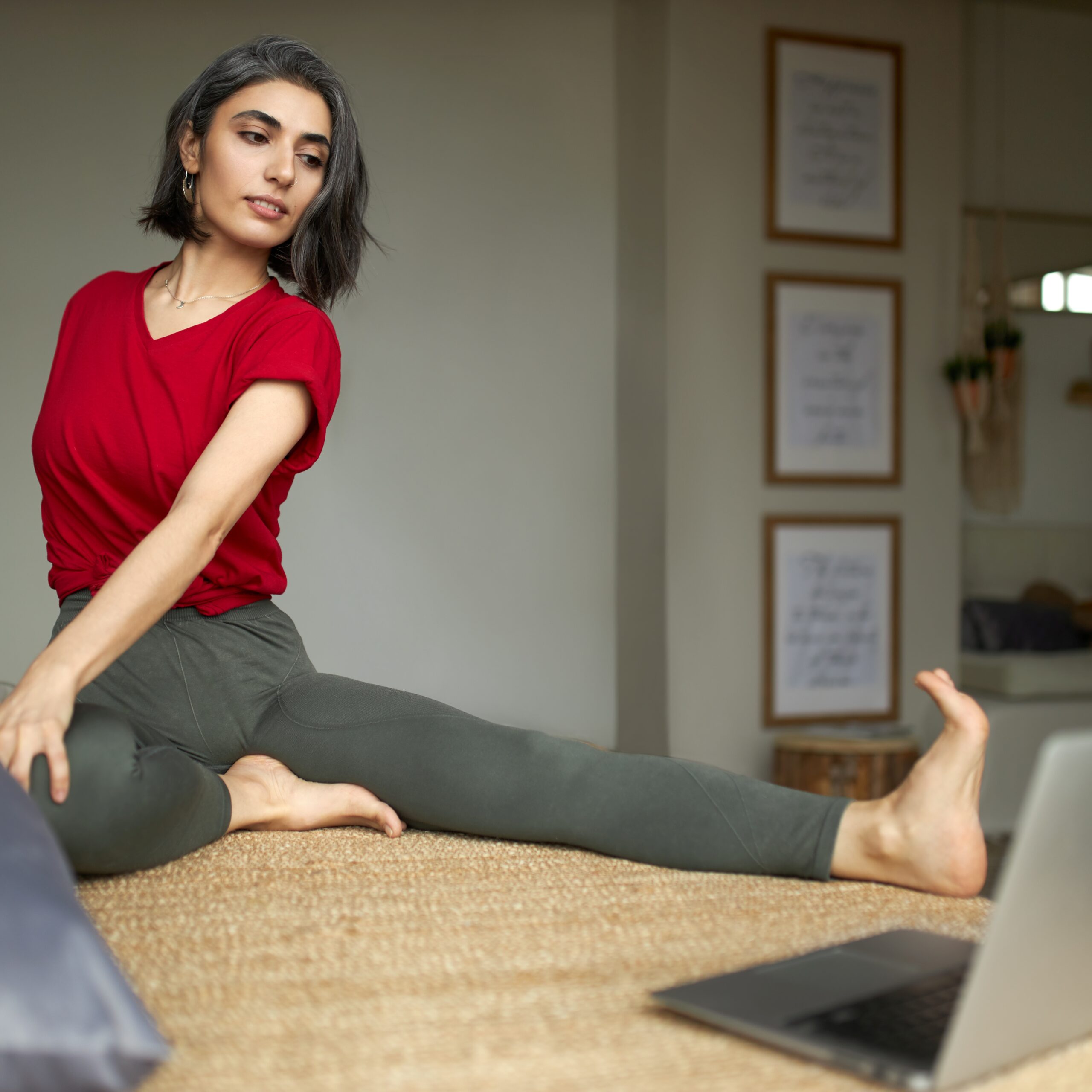 sporty flexible young woman with canities sitting floor strerching legs doing spinal twist looking computer screen watching online yoga video tutorial with step by step instructions